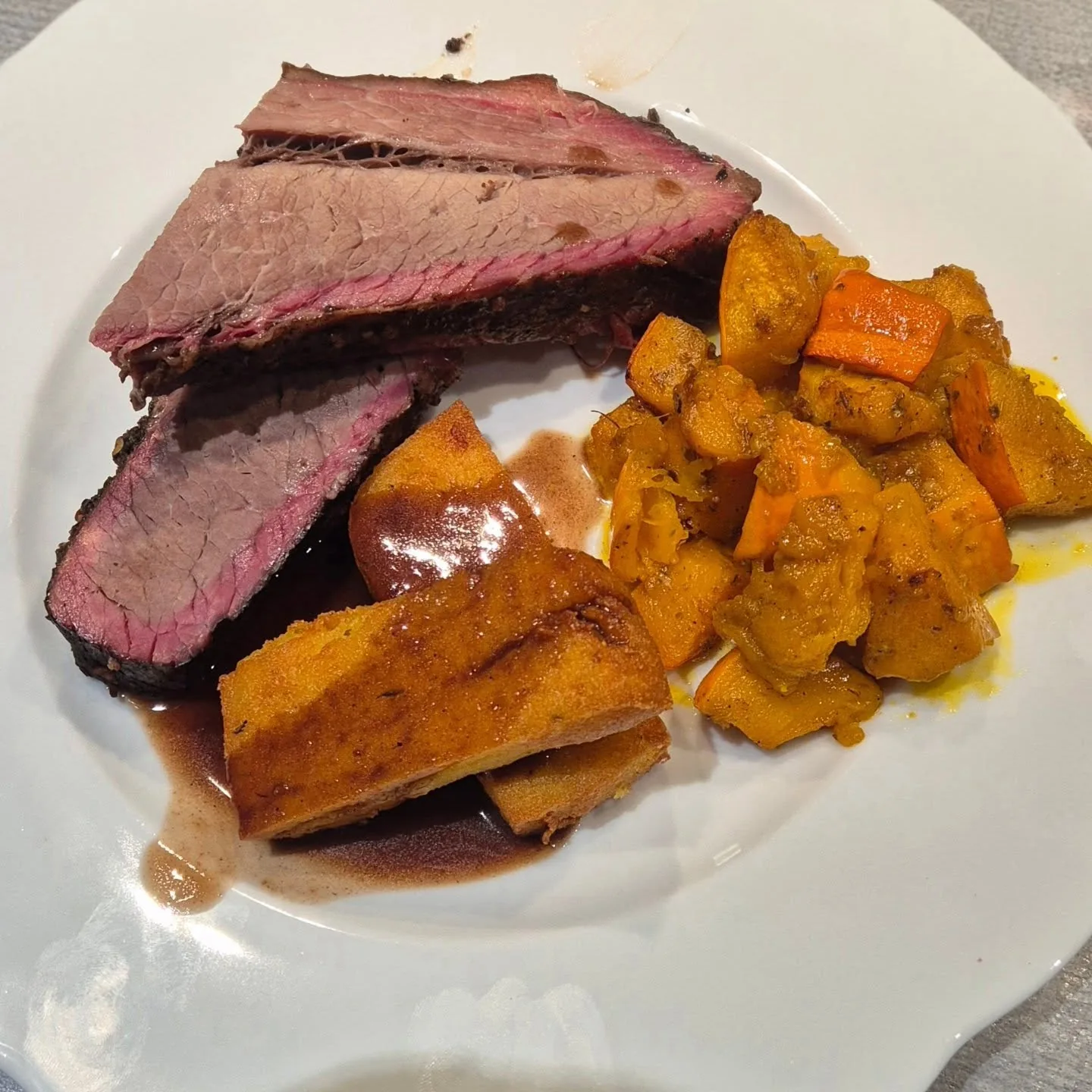 Aufgeschnittenes Brisket mit rosa Rauchrand, Kürbisgemüse, Polenta-Fritten und dunkler Soße auf einem weißen Teller