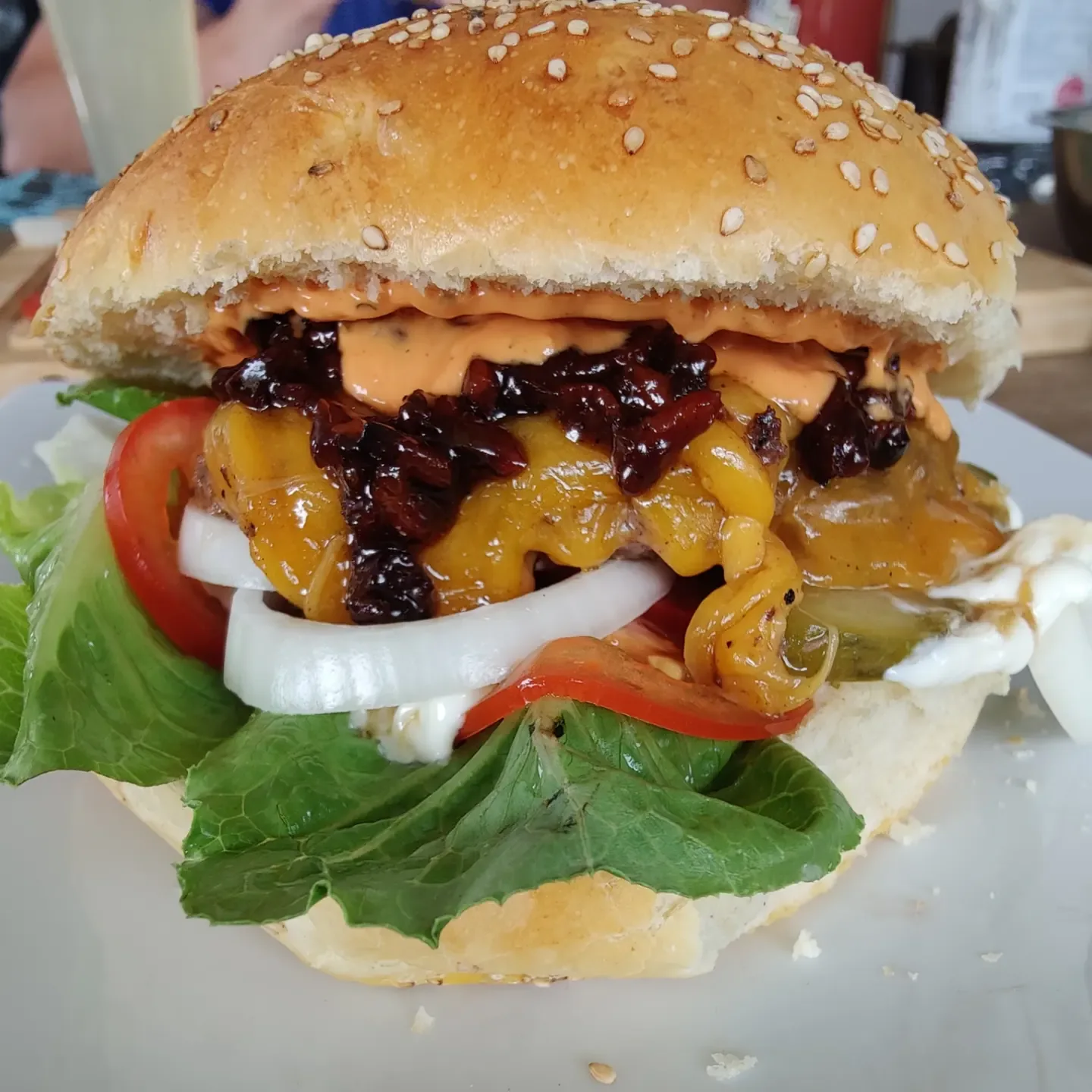 Cheeseburger mit geschmolzenem Käse, Baconjam, Zwiebeln, Tomate und Salat im Sesambrötchen