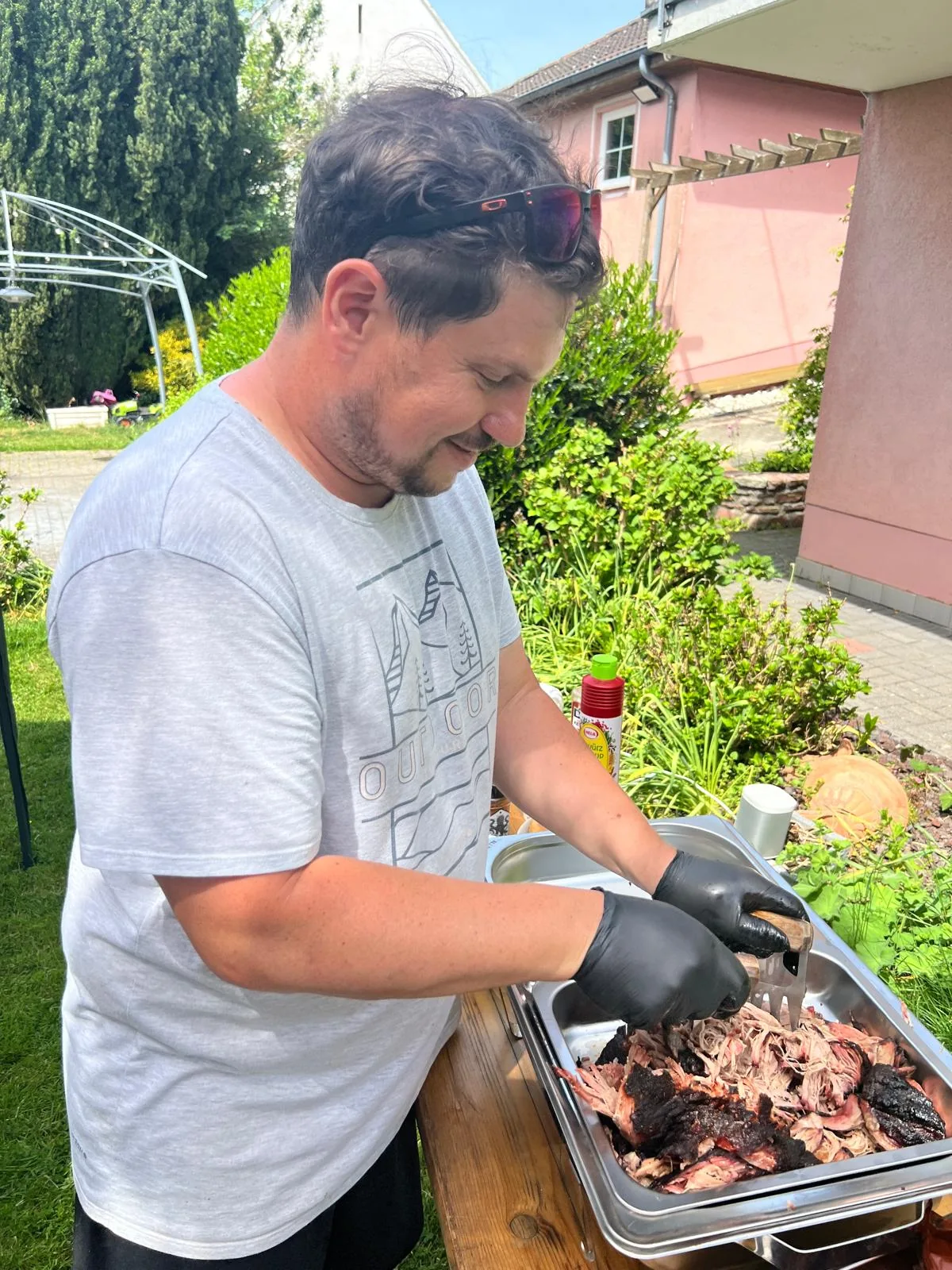 Christoph zerteilt im Garten mit Fleischkrallen Pulled Pork in einer Edelstahlschale