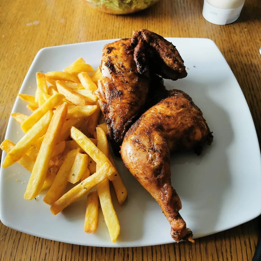 Gebräunte Hähnchenstücke mit knuspriger Haut und Pommes auf einem weißen Teller
