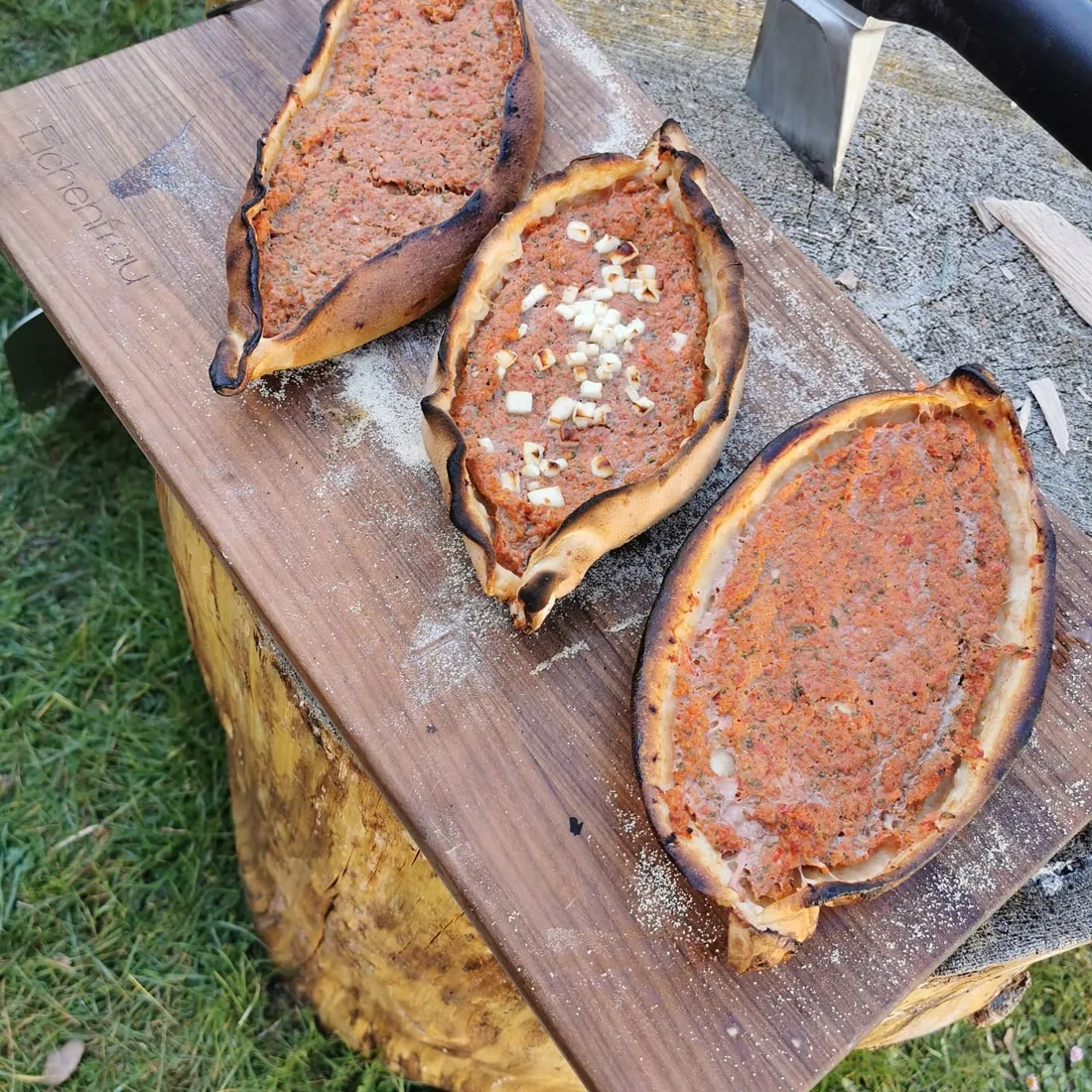 Drei längliche Pide mit würzigem Belag und gebräuntem Rand auf einem bemehlten Holzbrett