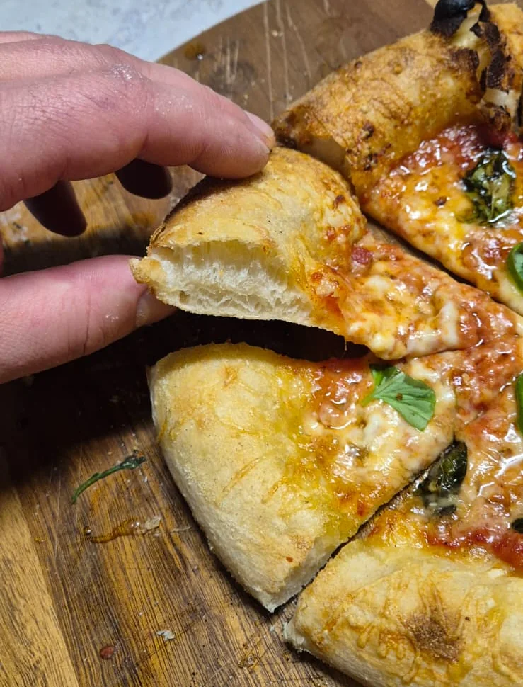 Belegte Pizza auf einem runden Pizzastein im Kugelgrill, dahinter und darunter offene Flammen
