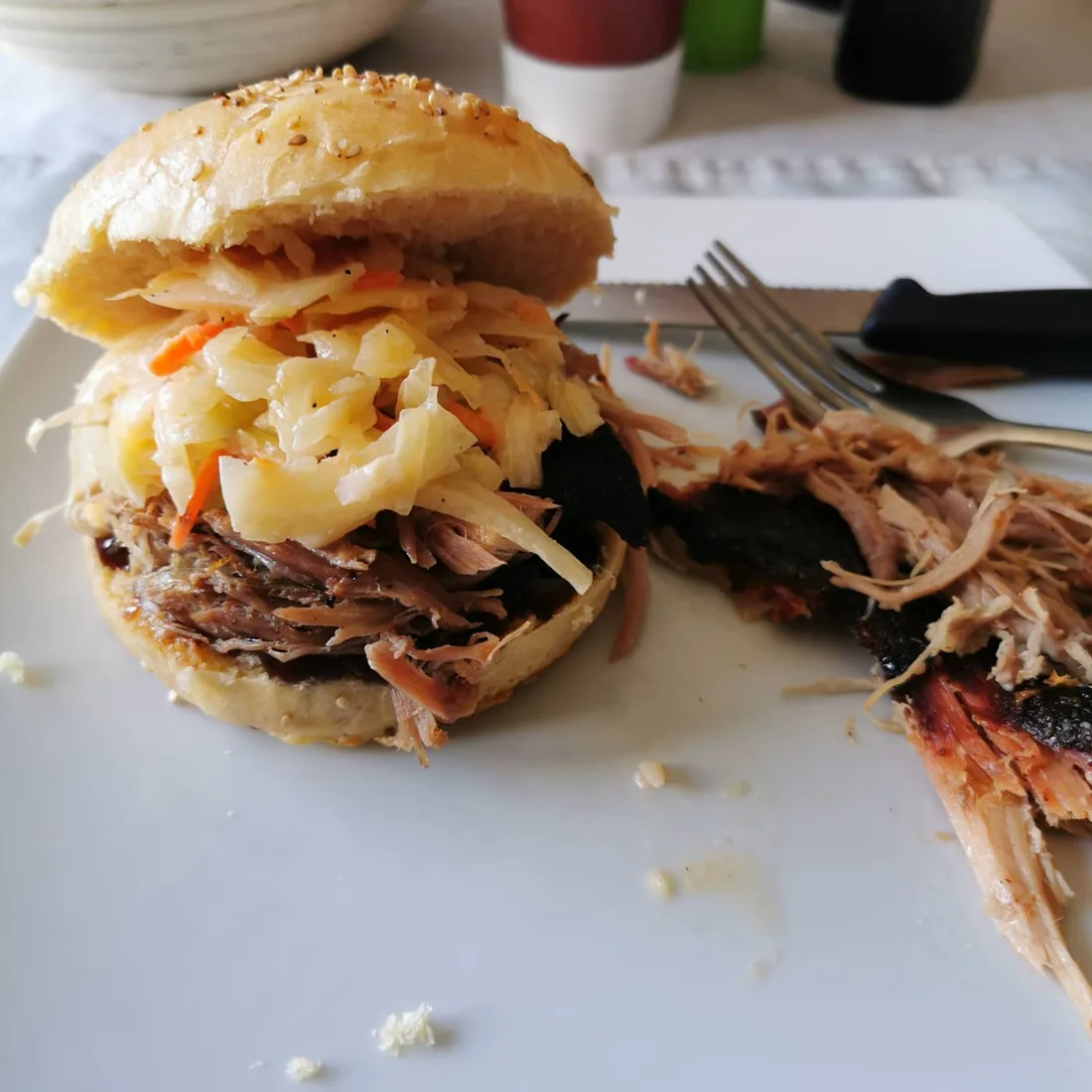 Pulled-Pork-Burger mit Krautsalat im Sesambrötchen und gezupftem Schweinefleisch auf einem weißen Teller