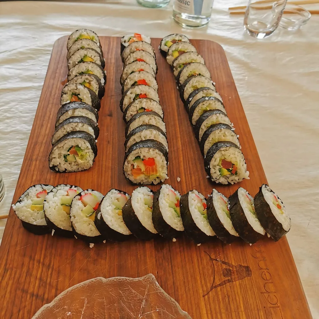 Mehrere Reihen selbst gerollter Maki mit verschiedenfarbigen Füllungen auf einem Holzbrett